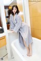 A woman in a bathrobe sitting on a bathtub in a bathroom.