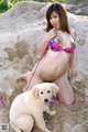 A woman in a bikini sitting in the sand next to a dog.