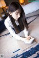 A woman sitting on the floor writing on a piece of paper.