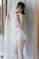 A woman in a white lingerie posing by a window.