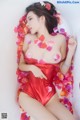 A woman in a red bathing suit laying in a bathtub covered in rose petals.