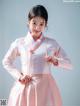 A woman in a pink and white hanbok poses for a picture.