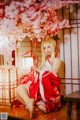 A woman in a red and white kimono sitting under a cherry blossom tree.