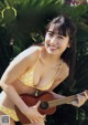 A woman in a yellow bikini holding a ukulele.