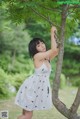 A woman in a white dress standing next to a tree.