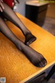 A woman in black stockings sitting on a wooden table.