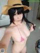 A woman in a bikini and a straw hat taking a selfie.