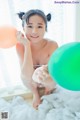 A naked woman sitting in a bathtub holding a green balloon.