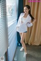 A woman in a white shirt and shorts posing by a window.