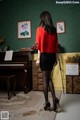 A woman in a red blouse and black skirt standing in front of a piano.