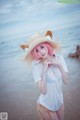 A woman with pink hair wearing a straw hat on the beach.