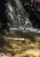 A naked woman floating in the water near a waterfall.