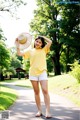 A woman in a yellow shirt and white shorts holding a straw hat.